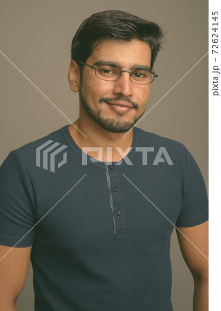 Young handsome bearded Persian man against gray background 72624145
