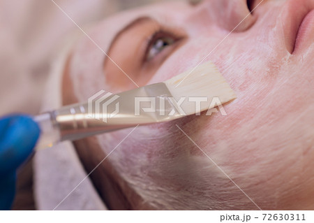 Spa concept. Young woman with nutrient facial mask in beauty salon, close up. The beautician applies a moisturizing mask to the client's face. 72630311