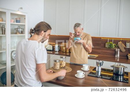 Smiling couple having coffee and talking in the kitchen Smiling couple having coffee and talking in the kitchen 72632496