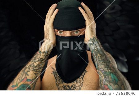 portrait of a guy in a balaclava with a bare torso in tattoos holding his head 72638046