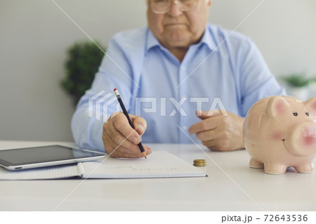 Elderly man in shirt in glasses sitting with calculator and piggybank for savings and making notes Elderly man in shirt in glasses sitting with calculator and piggybank for savings and making notes 72643536