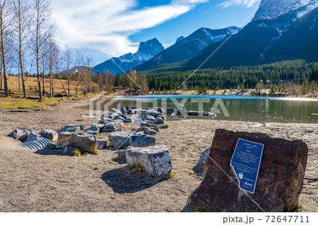 Quarry Lake park lakeshore in late autumn season sunny day morning. Snow capped Mount Lawrence Grassi mountains with blue sky in the background. Canmore, Alberta, Canada. Quarry Lake park lakeshore in late autumn season sunny day morning. Snow capped Mount Lawrence Grassi mountains with blue sky in the background. Canmore, Alberta, Canada. 72647711