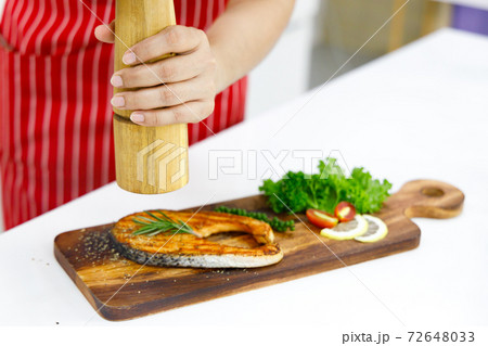 Chef sprinkle ground black pepper on grilled salmon steak. Concept chef preparing food before serving. Chef sprinkle ground black pepper on grilled salmon steak. Concept chef preparing food before serving. 72648033