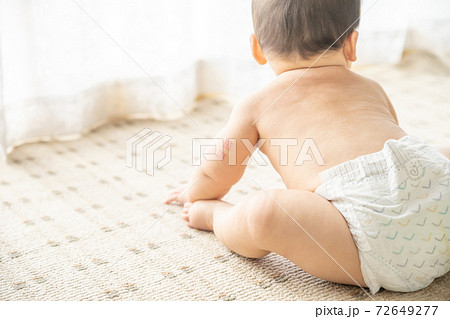 窓辺でお座りするオムツ姿の赤ちゃんの写真素材