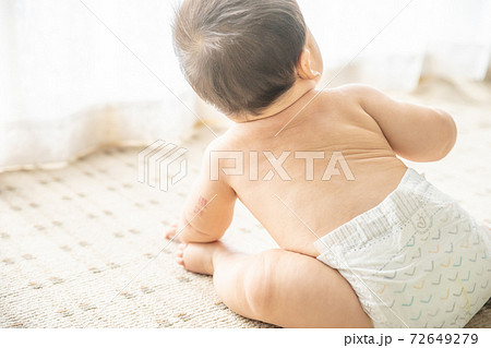 窓辺でお座りするオムツ姿の赤ちゃんの写真素材