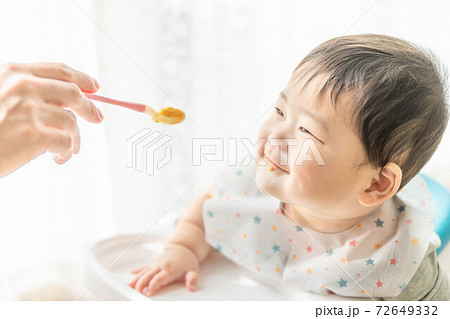 窓辺でベビーチェアに座って離乳食を食べる赤ちゃん 72649332