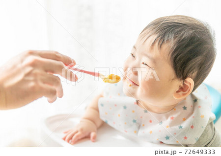 窓辺でベビーチェアに座って離乳食を食べる赤ちゃん 72649333
