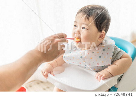 窓辺でベビーチェアに座って離乳食を食べる赤ちゃん 72649341