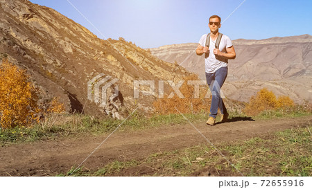 Man with sunglasses and backpack walks along narrow road Man with sunglasses and backpack walks along narrow road 72655916