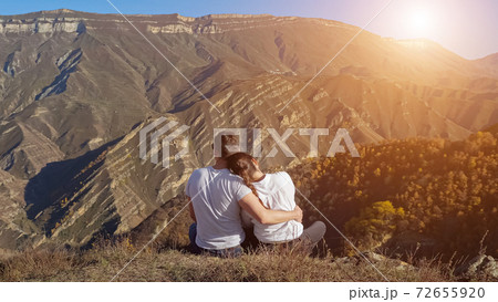 Man and woman hug on hill with dry grass against mountains 72655920