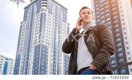 man in a leather jacket talking on the phone against the backdrop of tall houses man in a leather jacket talking on the phone against the backdrop of tall houses 72655939