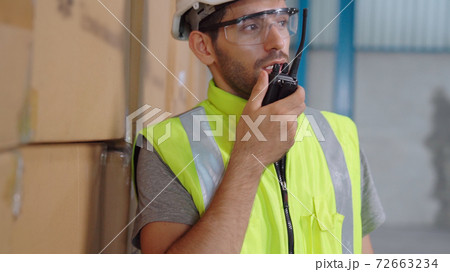 Professional cargo worker talks on portable radio to contact another worker Professional cargo worker talks on portable radio to contact another worker 72663234