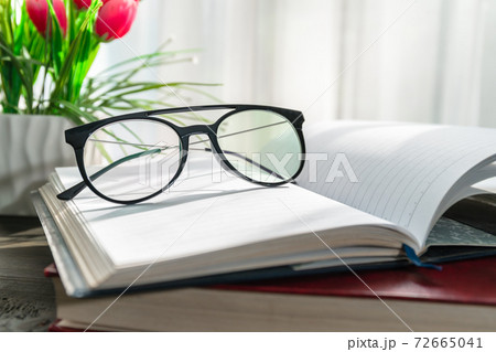 Reading glasses put on open book beside the window Reading glasses put on open book beside the window 72665041