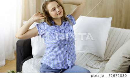 Happy blond woman put hands behind head sitting leaned on couch caucasian female enjoy lazy weekend or vacation in sunny living room 72672080