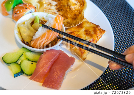 Closeup photo of human hands using chopsticks while eating sushi 72673329