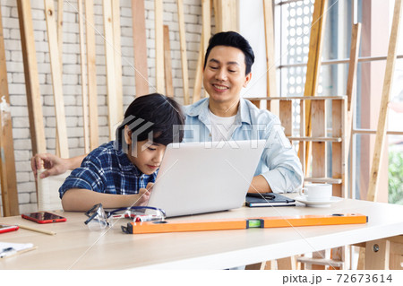 Asian father and son working together on laptop computer in carpentry workshop. Asian father and son working together on laptop computer in carpentry workshop. 72673614