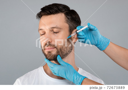 Attractive middle-aged man getting anti-aging procedure, grey background Attractive middle-aged man getting anti-aging procedure, grey background 72673889