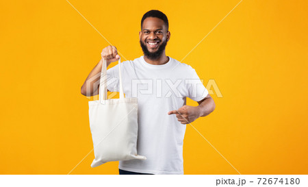 Smiling Black Guy Holding Eco Bag Standing Over Yellow Background Smiling Black Guy Holding Eco Bag Standing Over Yellow Background 72674180