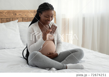 Sweet Tooth. Happy black pregnant woman enjoying eating chocolate in bed 72674251
