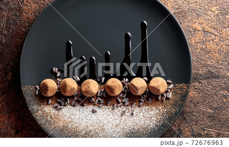 Chocolate truffles on a black plate with chocolate sauce. 72676963
