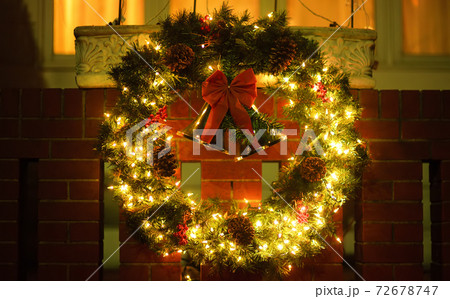 Christmas green wreath with red bells on the front door. Entrance to the house decorated for Xmas Christmas green wreath with red bells on the front door. Entrance to the house decorated for Xmas 72678747