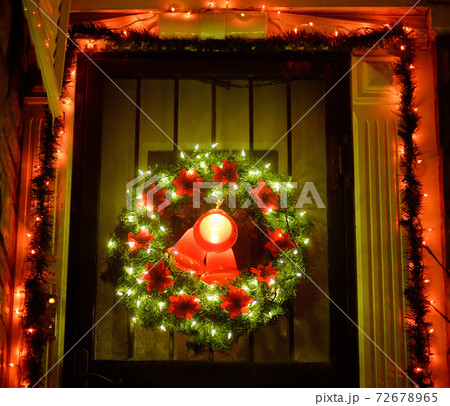 Christmas green wreath with red bells on the front door. Entrance to the house decorated for Xmas Christmas green wreath with red bells on the front door. Entrance to the house decorated for Xmas 72678965