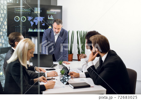 Mature male chief leans on the table and talking with his team, professional successful multiethnic male and female colleagues, working together over joint strategy of company Mature male chief leans on the table and talking with his team, professional successful multiethnic male and female colleagues, working together over joint strategy of company 72683025