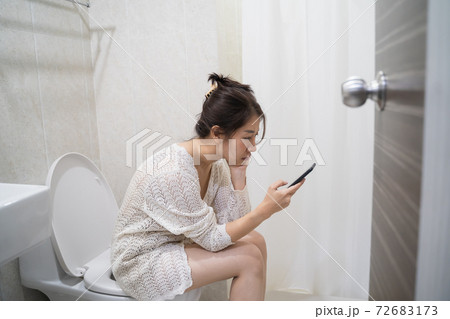 asian woman on toilet with cell phone. Woman sitting with mobile in toilet 72683173