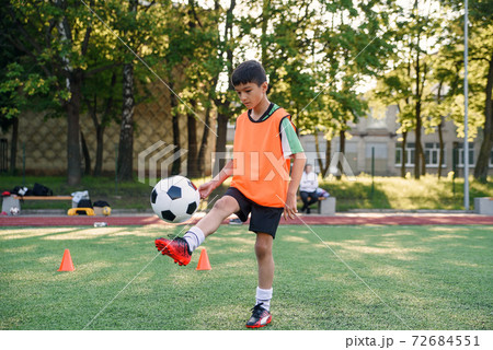 Motivated teen football player stuffs soccer ball on leg. Practicing sport exercises at artificial stadium. 72684551
