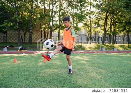 Motivated teen football player stuffs soccer ball on leg. Practicing sport exercises at artificial stadium. 72684552