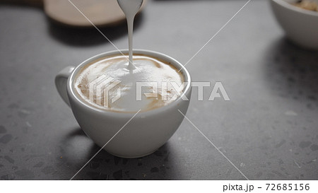 Pour steamed milk into espresso to make cappuccino on concrete countertop closeup 72685156