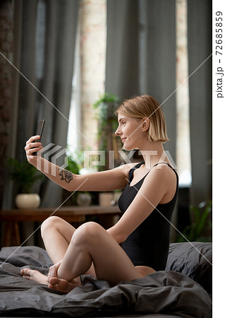 Happy young female in black leotard making selfie on bed in the morning Happy young female in black leotard making selfie on bed in the morning 72685859