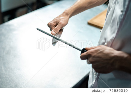 Hands of young male chef of modern restaurant in white uniform sharpening knife Hands of young male chef of modern restaurant in white uniform sharpening knife 72686010