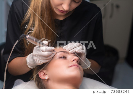 Permanent eyebrow makeup. Cosmetologist applying tattooing of eyebrows. 72688242