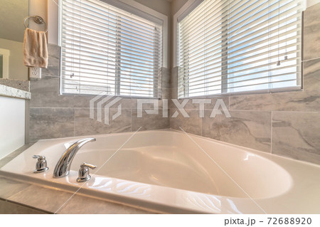 Close up of clean built in bathtub inside a bathroom with windows and tile wall Close up of clean built in bathtub inside a bathroom with windows and tile wall 72688920