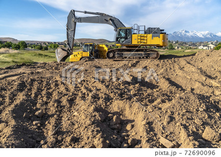 Yellow construction vehicles at a construction site against mountain and sky Yellow construction vehicles at a construction site against mountain and sky 72690096