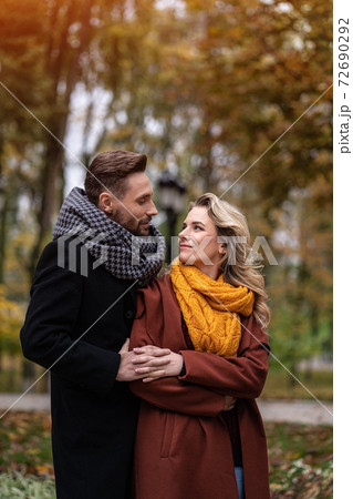 Handsome man and a woman hugged from behind smile looking at each other in the autumn park. Outdoor shot of a young couple in love having great time. Autumn toned image Handsome man and a woman hugged from behind smile looking at each other in the autumn park. Outdoor shot of a young couple in love having great time. Autumn toned image 72690292
