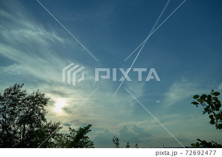 Jet smoke and deep blue sky white clouds behind trees 72692477