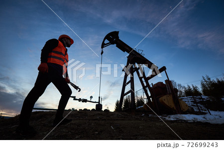 Oil man standing by pump jack under blue evening sky. Oil man standing by pump jack under blue evening sky. 72699243
