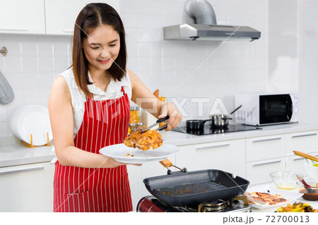 Asian woman chef putting cooked pork steak on plate. Concept woman preparing meals at home. Asian woman chef putting cooked pork steak on plate. Concept woman preparing meals at home. 72700013