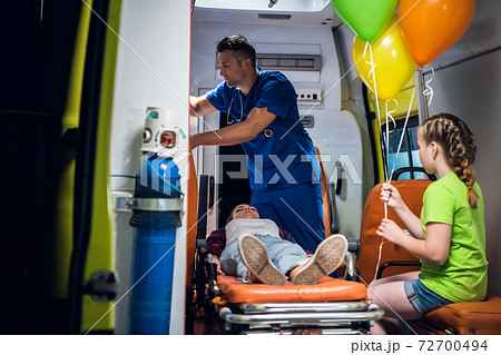 Unconscious mother lying on a stretcher in an ambulance car, a paramedic providing her first aid Unconscious mother lying on a stretcher in an ambulance car, a paramedic providing her first aid 72700494