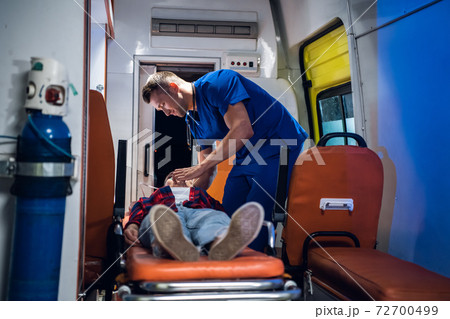A young paramedic in a uniform gives an oxygen mask to his patient A young paramedic in a uniform gives an oxygen mask to his patient 72700499