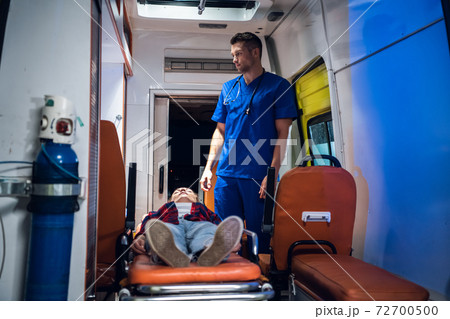 Unconscious woman lying on a stretcher in an ambulance car, a paramedic providing her first aid 72700500