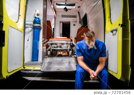 Man in a medical uniform sitting in the ambulance car at night Man in a medical uniform sitting in the ambulance car at night 72701456