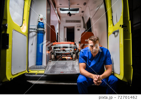 Serious man in a medical iniform sitting in the back of an ambulance car Serious man in a medical iniform sitting in the back of an ambulance car 72701462