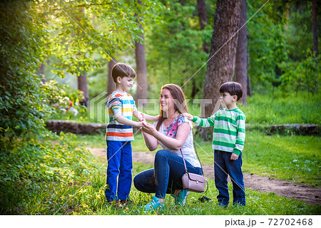 Young woman mother applying insect repellent to her two son before forest hike beautiful summer day or evening. Protecting children from biting insects at summer. Active leisure with kids Young woman mother applying insect repellent to her two son before forest hike beautiful summer day or evening. Protecting children from biting insects at summer. Active leisure with kids 72702468