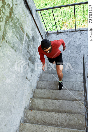 Concentrated male athlete running up stairs to make training more intensive. Sporty handsome young man training alone outdoors. Staircase workout concept 72703117