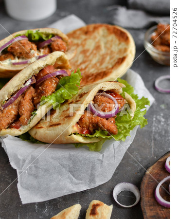Lavash salad with fried chicken and vegetables. Pita with chicken nuggets, tomatoes, red onions and lettuce and sauce. Healthy fast food. Dark background. Vertical view Lavash salad with fried chicken and vegetables. Pita with chicken nuggets, tomatoes, red onions and lettuce and sauce. Healthy fast food. Dark background. Vertical view 72704526