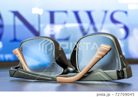 The eyeglasses lie on the table in front of the television with TV news. 72709045