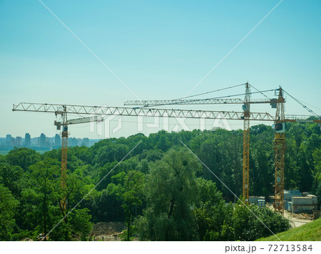 Construction cranes on the outskirts of the city. Destruction of forests by construction. Construction cranes on the outskirts of the city. Destruction of forests by construction. 72713584